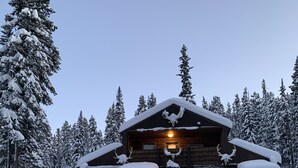 A wooden cabin with a porch, surrounded by snow-covered trees.