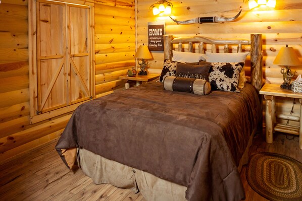 A log cabin-style bedroom with a bed, wooden walls, a 'HOME' sign, and a cow head decoration. - Hunting Cabin w/ Air Purifier (Branson)