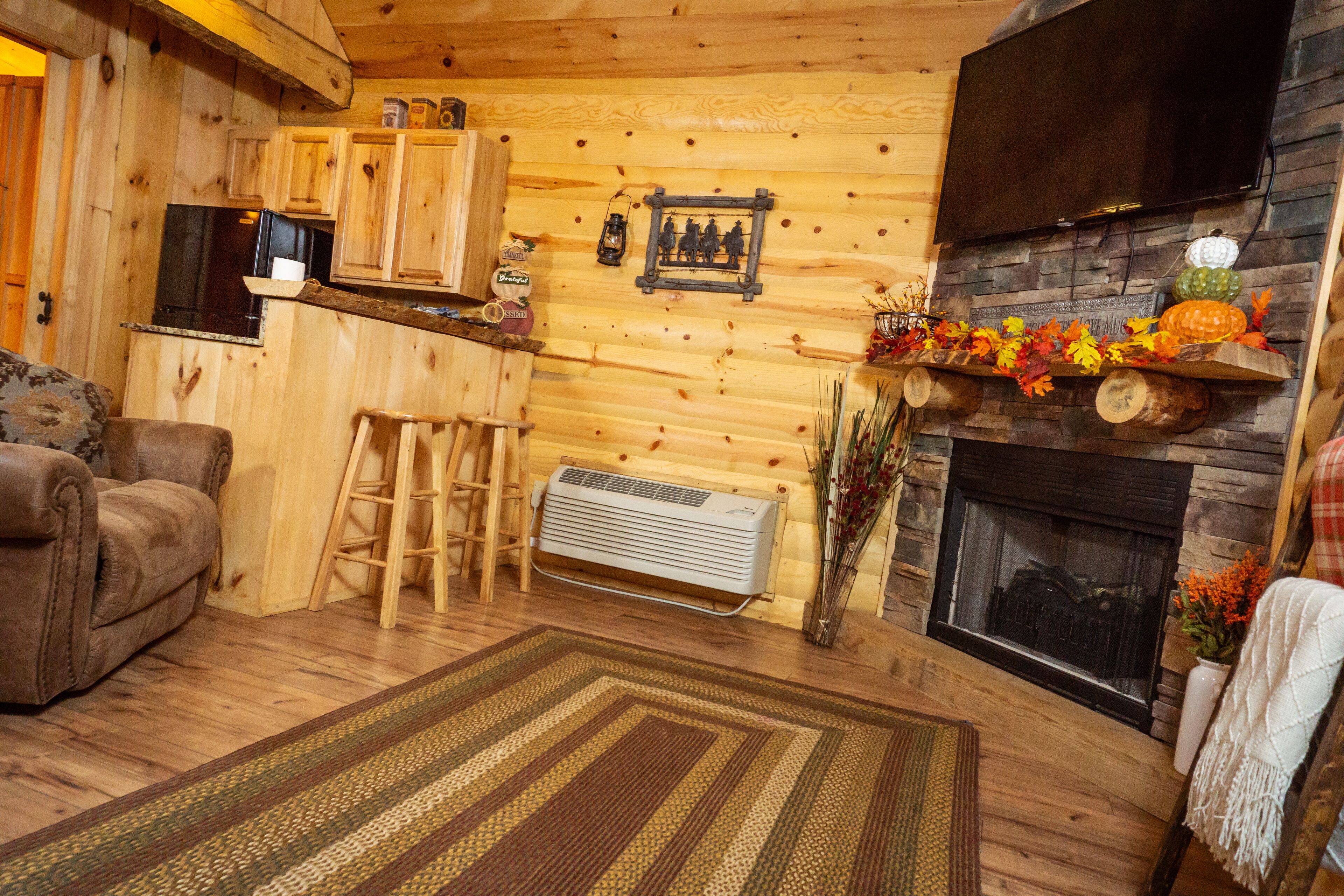 A cozy log cabin interior with a fireplace, wooden walls, a sofa, a ladder, and a TV mounted above the fireplace.