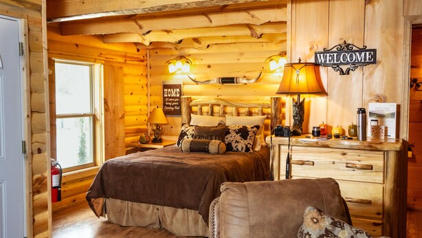 Een slaapkamer in een blokhut met twee bedden, een bank, een houten trap en een welkom bord.