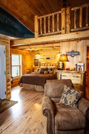 A log cabin bedroom with two beds, a sofa, a wooden staircase, and a welcome sign. - Hunting Cabin w/ Air Purifier (Branson)