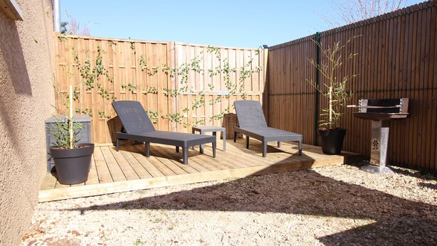 Une terrasse avec deux fauteuils de jardin, une petite table et un pot de fleurs.