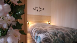 Une chambre avec un lit, un mur décoré d’un motif d’oiseau et une plante aux fleurs blanches.
