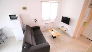 Un salon moderne comprenant un canapé, une table basse, un téléviseur et une petite kitchenette.