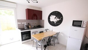 Une cuisine compacte avec une table en bois, des chaises grises, un réfrigérateur blanc et une œuvre d’art noire accrochée au mur.