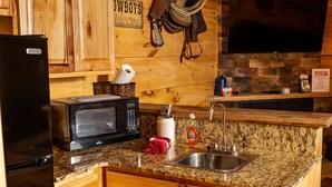 Una cocina con armarios de madera, un refrigerador negro, un microondas, un lavamanos y un salpicadero de piedra.