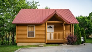 Una pequeña cabaña de madera con techo de metal rojo, un porche y un buzón.