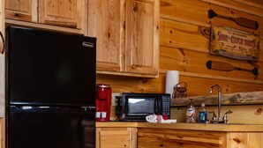 Una cocina con armarios de madera, un refrigerador negro, un microondas y una cafetera.