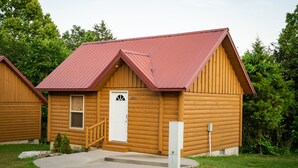 Una cabaña de troncos con techo metálico rojo, una puerta principal y un pequeño porche.