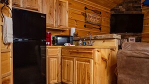 Una cocina compacta con muebles de madera, un refrigerador negro, un microondas y un lavamanos.
