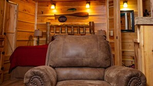 Interior de una cabaña de madera con una silla de cuero, paredes de madera y una colcha roja.