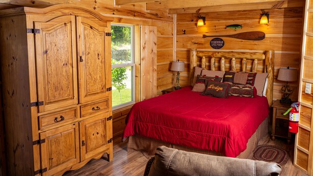 Un dormitorio tipo cabaña de madera con una cama grande, un armario y una ventana.