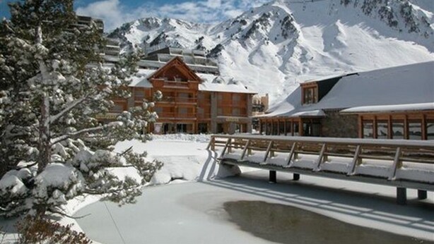 Un refugio de montaña cubierto de nieve con fachada de madera y un telesilla al fondo.