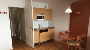 Cocina compacta equipada con microondas, hervidor y lavavajillas. Cuenta con una mesa de comedor con sillas y una pequeña mesa de madera.