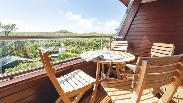 A wooden deck with a table and chairs, overlooking a scenic landscape with hills and a body of water. - Kliffhoog 5 from A&M - Kliffhoog 5 (Kampen (Sylt))