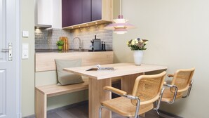 A compact kitchen with a built-in bench and two wicker chairs, a coffee machine, and a vase with flowers on the counter. - Kliffhoog 5 from A&M - Kliffhoog 5 (Kampen (Sylt))