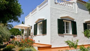 Un edificio blanco con contraventanas verdes, un balcón y un patio con mobiliario exterior.