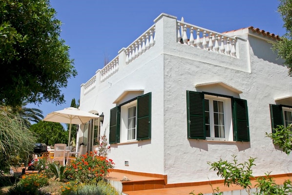 Un bâtiment blanc avec des volets verts, un balcon et un patio aménagé avec du mobilier d’extérieur.