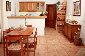 Une cuisine avec des meubles de rangement en bois, une table à manger avec des chaises et un petit îlot central doté d’un évier.