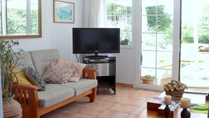 Una sala de estar con sofá, televisión y plantas en macetas.