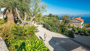 A coastal garden with stone pathways, lush greenery, and a view of the sea. - 1 bedroom amazing apartment in Ravni (Ravni)