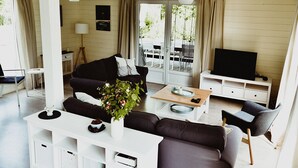 Een moderne woonkamer met een bank, salontafel en tv-meubel. Er is een raam met gordijnen, een lamp en een plant.