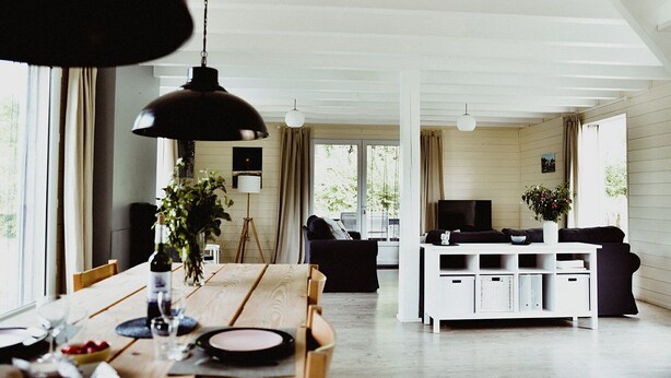 Een ruime woonkamer met een houten eettafel, zwart-wit meubels en grote ramen die natuurlijk licht binnenlaten.