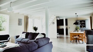 Een ruime woonkamer met een donkergrijze bank, een eettafel met stoelen en een keuken op de achtergrond.