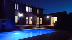 Een zwembad met een houten terras, een overdekte zithoek en een kleine tafel met glazen en een kaars.