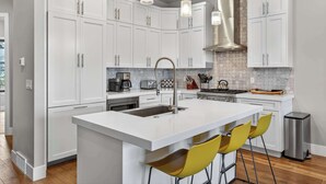 Una cocina moderna con armarios blancos, una isla central con taburetes de bar, electrodomésticos de acero inoxidable e iluminación colgante.