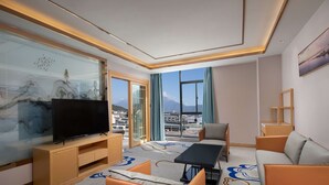 A hotel room with a large flat-screen TV, a sofa, a coffee table, and a view of the city through large windows. - Microtel by Wyndham Lijiang (Lijiang)