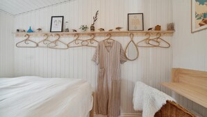 Un dormitorio con cama, perchero, cesta de mimbre y estante con adornos.