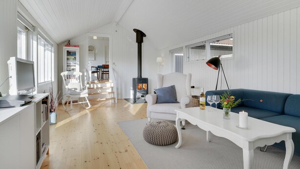 Amplia sala de estar con un sofá blanco, una mesa de centro y una chimenea. Hay un televisor sobre un mueble bajo y una estantería al fondo.