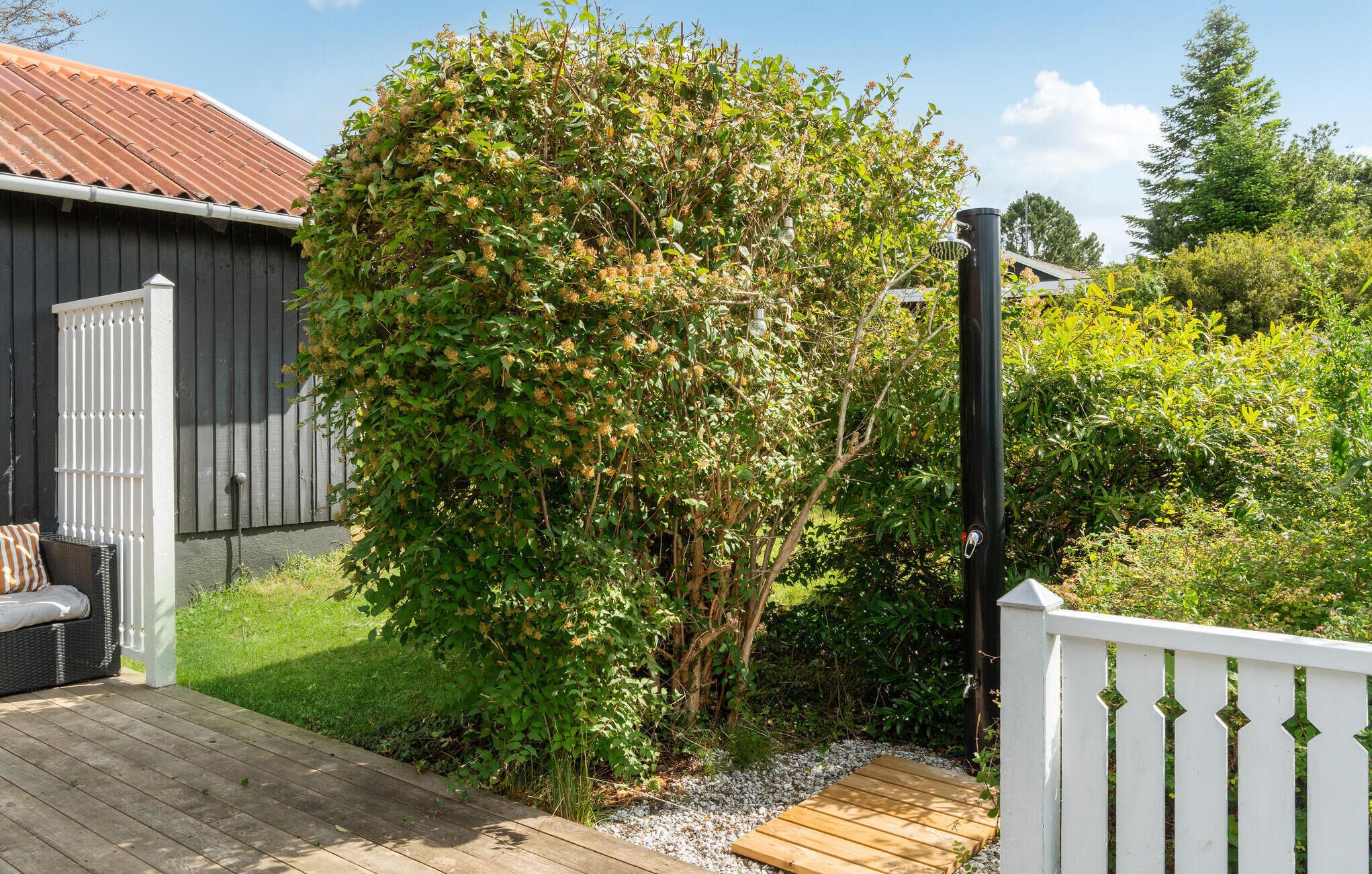 A wooden deck with a white fence, a small garden area with a tree, and a shed with a red roof.
