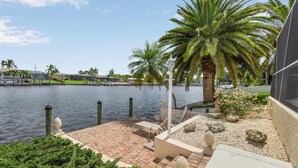 A waterfront patio with a palm tree, a lamp post, and a view of the water. - Holidays in Paradise! NO bridges, NO locks to the Gulf of Mexico! (Cape Coral)