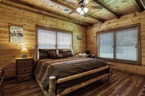 A wooden cabin bedroom with a bed, nightstands, a ceiling fan, and large windows.