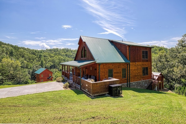 A large wooden cabin with a green roof, a covered porch, and a stone foundation.
