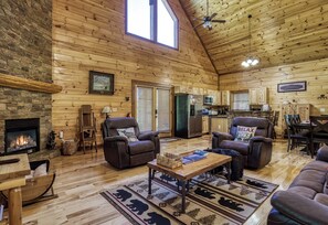 A spacious living room with a fireplace, wooden walls, and a high ceiling.
