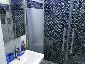 Ein Badezimmer mit weißem Waschbecken, einem Spiegel und einer Dusche mit schwarzem Fliesenbelag.