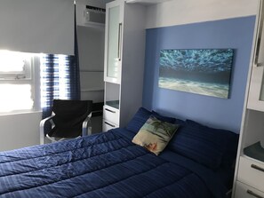 Ein Schlafzimmer mit Bett, Schreibtisch und Stuhl. An der Wand hängt ein Gemälde und das Fenster ist mit Vorhängen versehen.