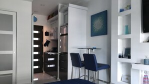 Un dormitorio moderno con cama, escritorio con sillas, armario y estante con objetos decorativos.