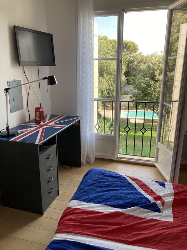 A bedroom with a bed, a desk, a television, and a balcony with a pool view.