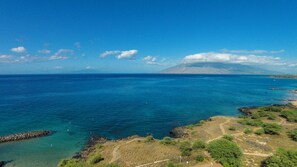 A coastal landscape with clear blue waters, rocky shorelines, and a distant mountain.