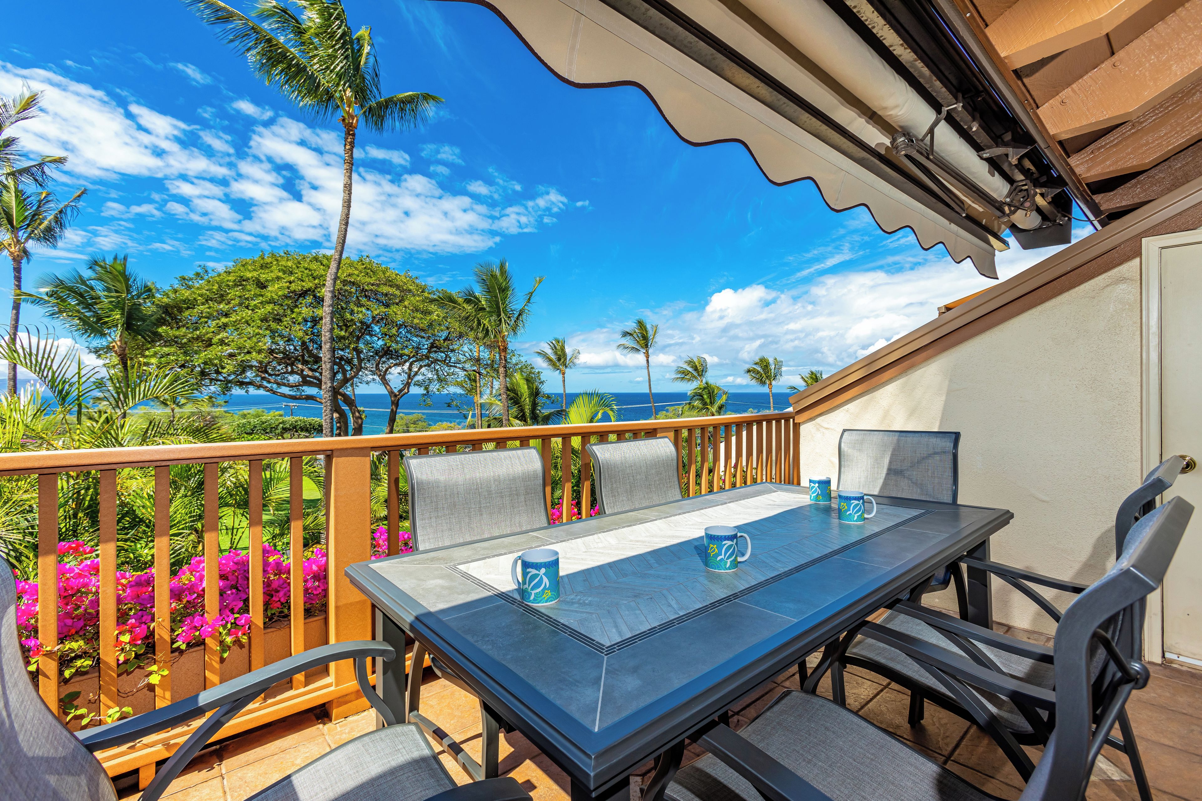 A balcony with a table and chairs, overlooking a beach with palm trees and a clear sky.