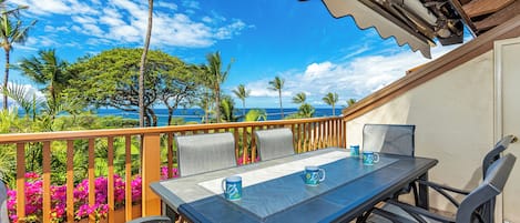 A balcony with a table and chairs, overlooking a beach with palm trees and a clear sky.