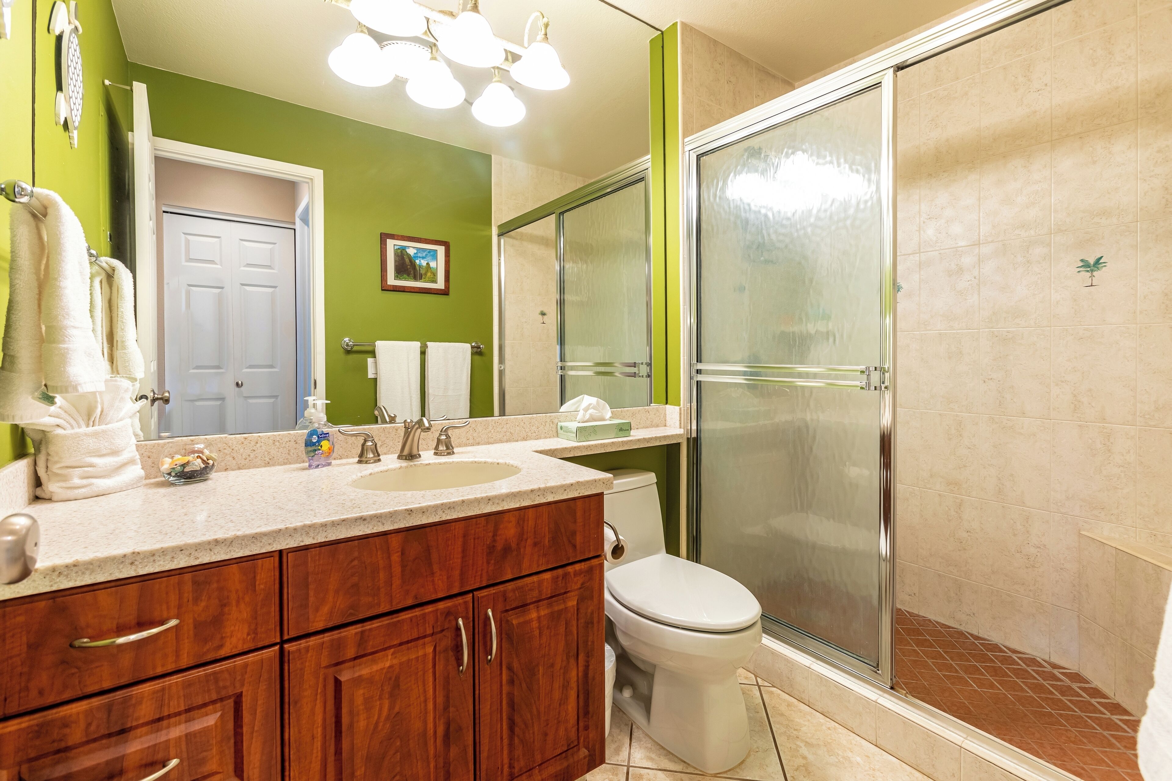 A bathroom with a wooden vanity, two sinks, a toilet, and a glass-enclosed shower.