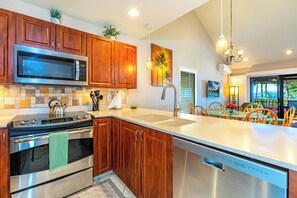 A modern kitchen with wooden cabinets, stainless steel appliances, a large island with a sink, and a dining area with chairs and a table.