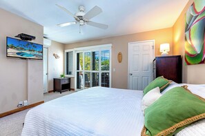 A bedroom with a large bed, a ceiling fan, a TV mounted on the wall, and a window with shutters. - Maui Kamaole #G-201 Front Row, Ocean View, Full A/C, Hot Tub, Great Rates (Kihei)