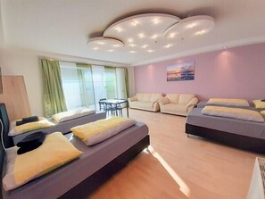 A modern hotel room with a sofa bed, a separate bed, a dining area, and a large window with curtains. - Apartments SteelCity Linz (Linz)