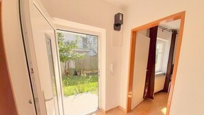 Un couloir avec une porte-fenêtre coulissante donnant sur une cour arrière où se trouvent un arbre et une clôture.